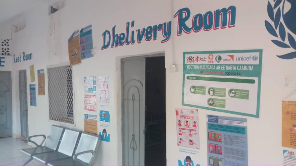 Delivery room painted over doorway of a white building information posters on the wall to the right of the doorway, sofa on the left hand side